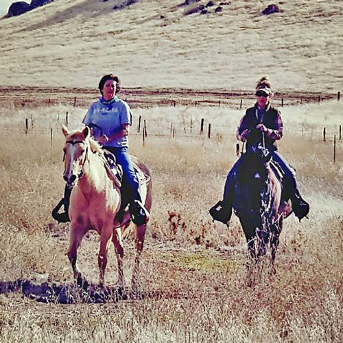 Two ladies riding horses through a field